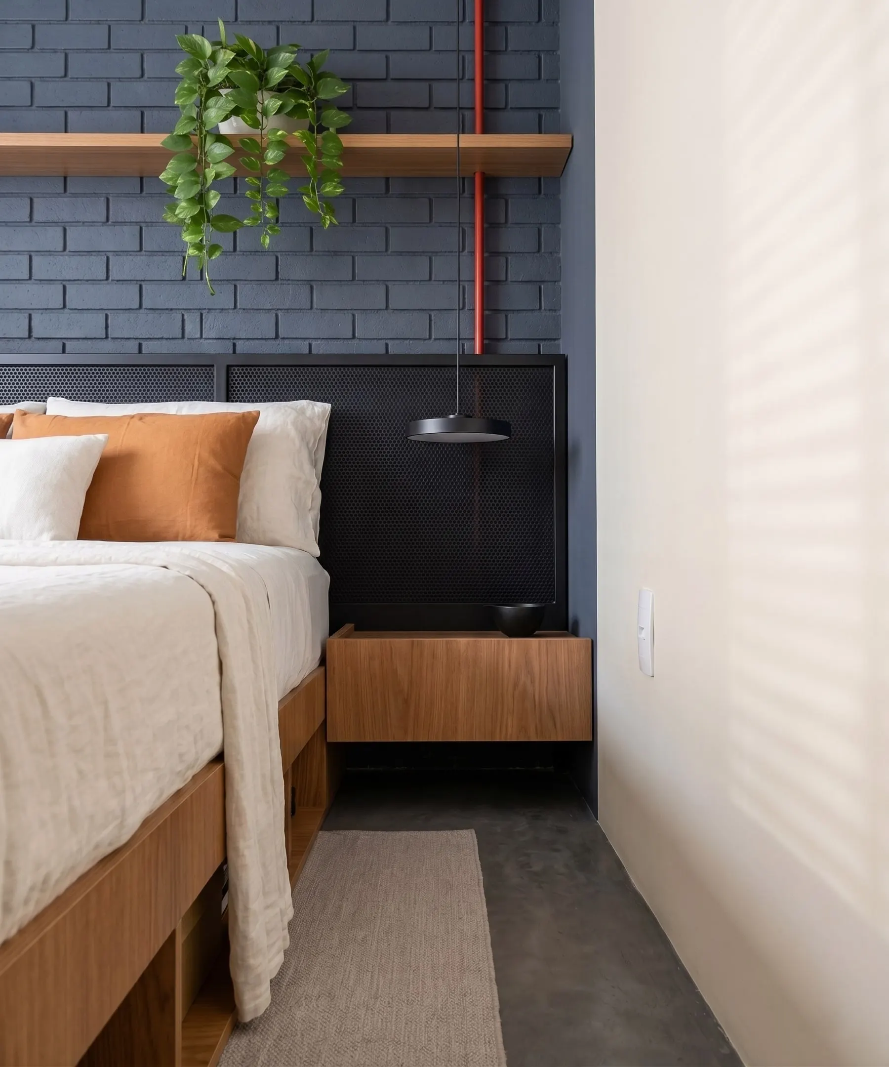 Quarto com parede de tijolos azuis, cabeceira preta e roupa de cama clara